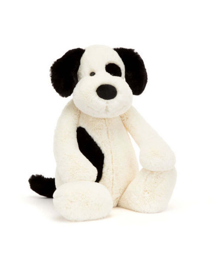 The Jellycat Bashful Rufferty Black + Cream Puppy Really Big is a plush stuffed animal with cream fur, black ears and tail, a patch over one eye, and a side spot, shown sitting upright against a white background.