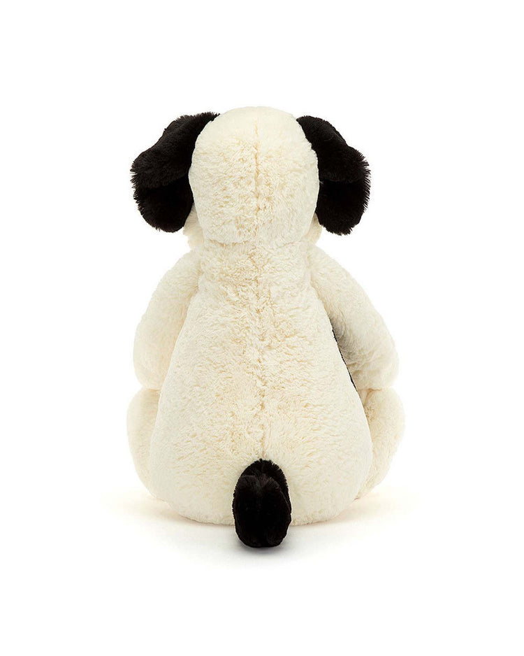 The Jellycat Bashful Rufferty Black + Cream Puppy Really Big plush sits with its back turned, showing off soft cream-colored fur and black ears and tail against a plain white background.