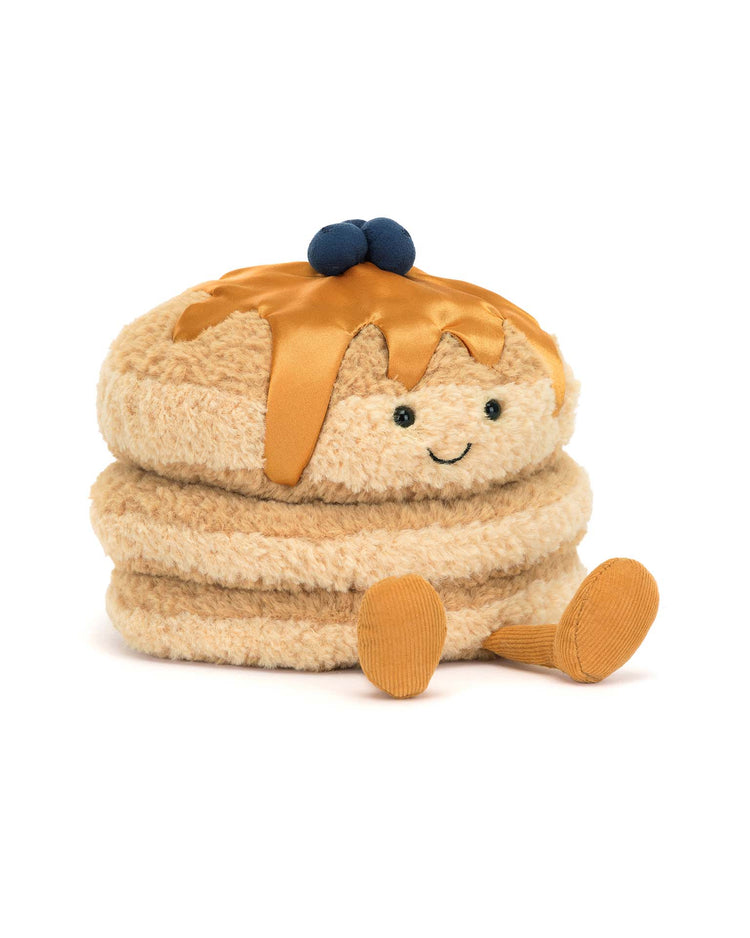The Jellycat Amuseables Fran Pancakes plush toy looks like a stack of pancakes with syrup. It has a smiling face, small feet, and textured blueberries on top. Its fluffy golden fur makes it irresistibly cuddly and delightful to hold.