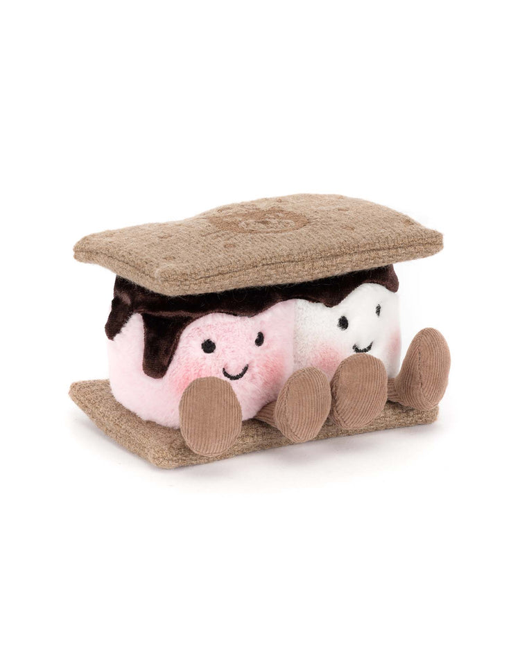Jellycat’s Amuseables S’mores is a plush toy featuring two smiling marshmallows—one pink, one white—nestled between soft brown crackers and chocolate, each with cute faces and dangling legs.
