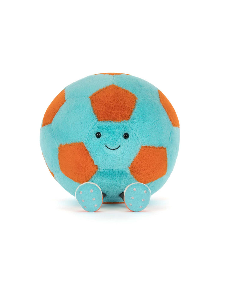The amuseables jellycat soccer ball by Jellycat is a kids’ plush shaped like a soccer ball with orange and blue patches, a smiling face, and small blue feet with orange spots, sitting upright on a white background.