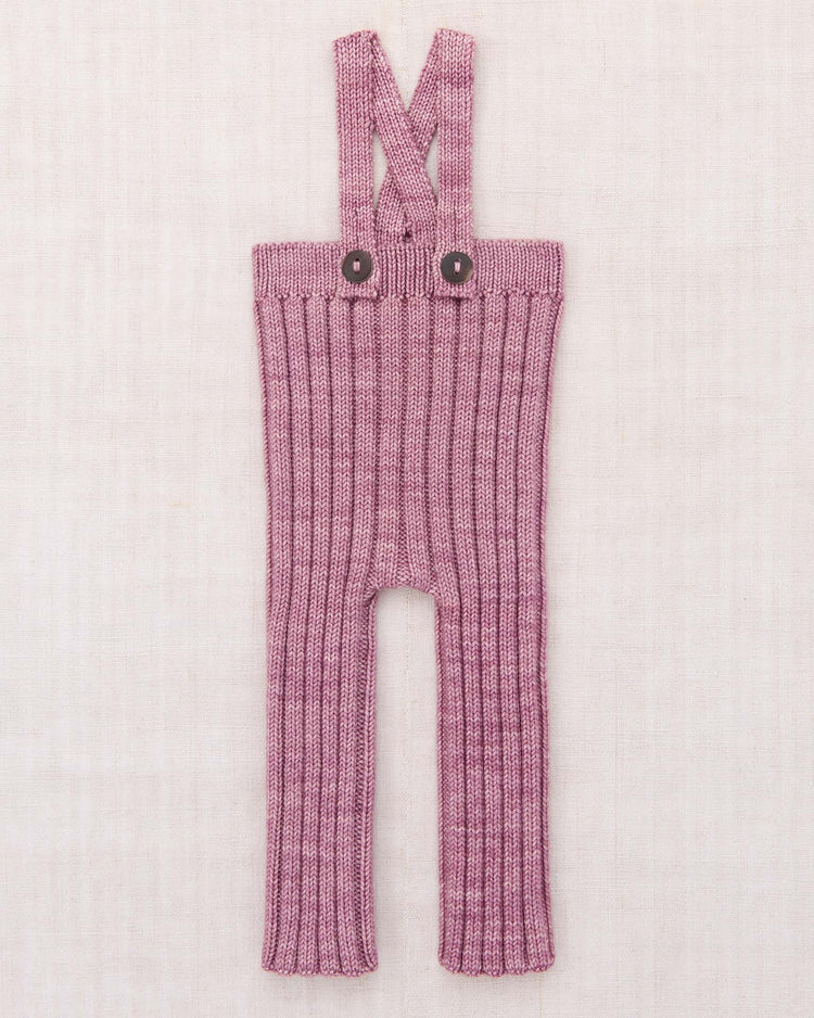 The "baby rib longies in antique rose" by misha + puff feature a ribbed texture, long legs, and two adjustable straps that cross at the back. Crafted from soft Merino wool knit, the straps fasten to the waistband with two dark buttons. The overalls are shown laid flat on a light background.