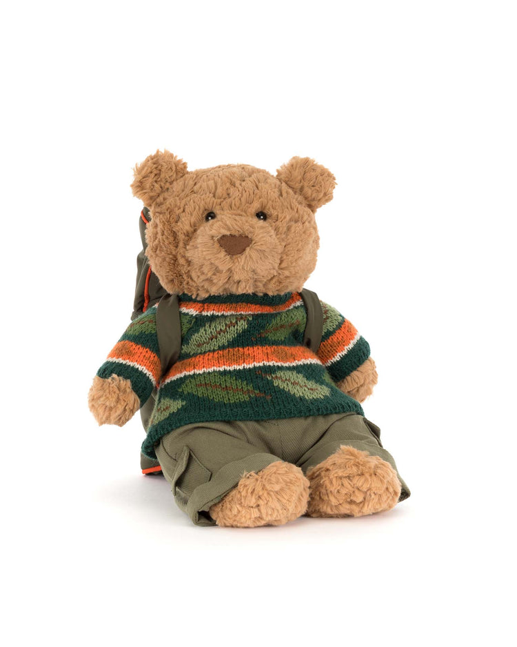 Bartholomew Bear from Jellycat, dressed in the Hiking Outfit—green, orange, and striped sweater with green pants and a matching backpack—sits against a white background.