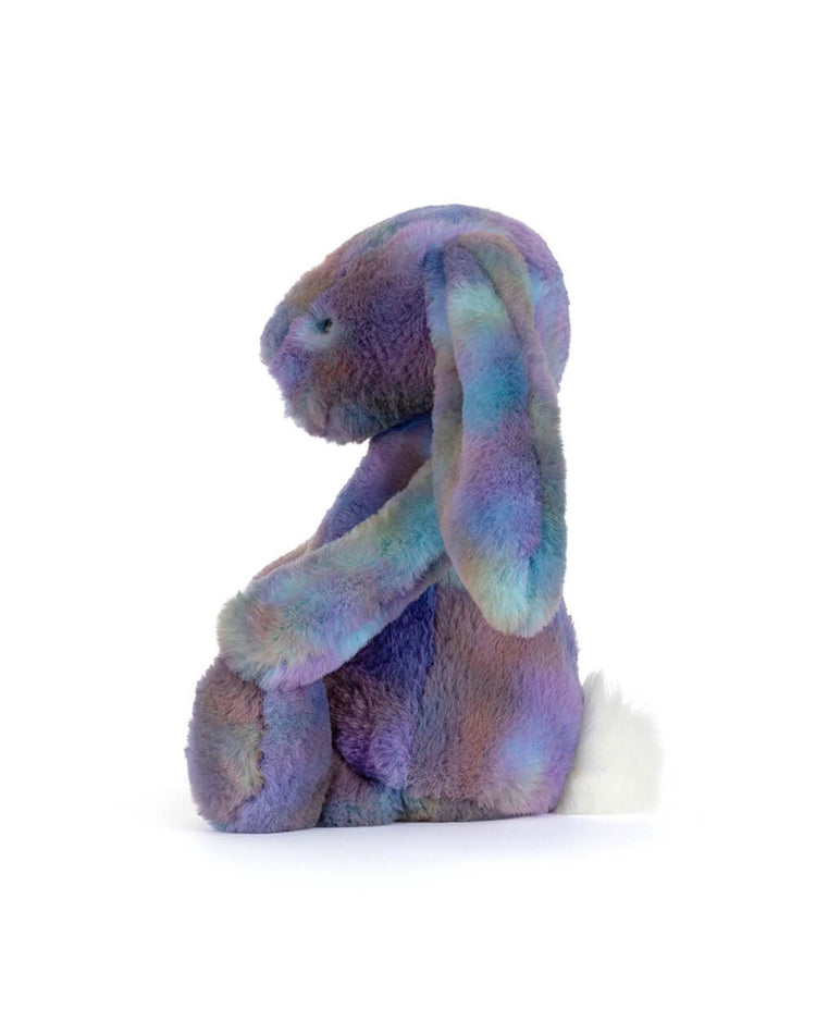 The Jellycat Zodihop Luxe Bunny plush features soft, multicolored fur in purple, blue, and green. It sits upright facing left with long floppy ears and a small white tail on a plain white background.