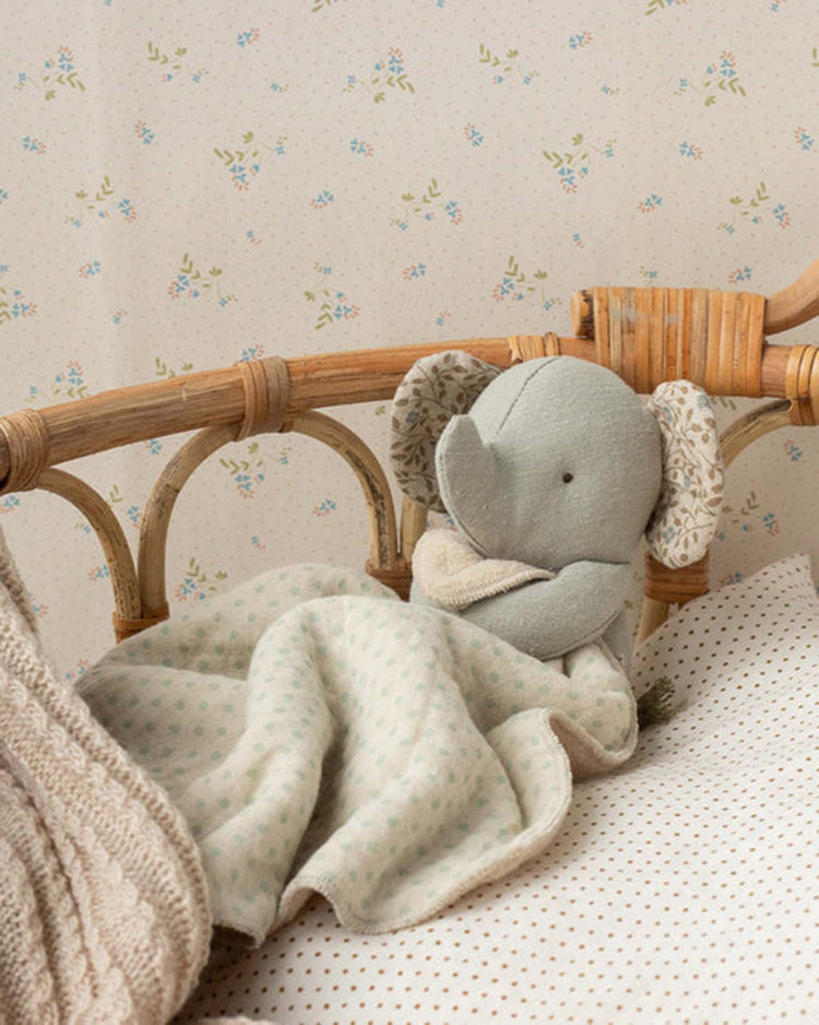 The maileg lullaby friends, elephant, mini - iron grey, with patterned ears, sits on a crib wrapped in a light green polka dot blanket beside a beige one—a charming touch for any softly decorated nursery and an ideal gift for newborns.