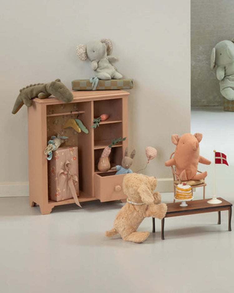 A small cabinet holds huggable stuffed animals, including the maileg mini crocodile in olive green from the safari friends collection. More plush toys gather at a tiny table with a cake and Danish flag, while another elephant plush appears in the background.