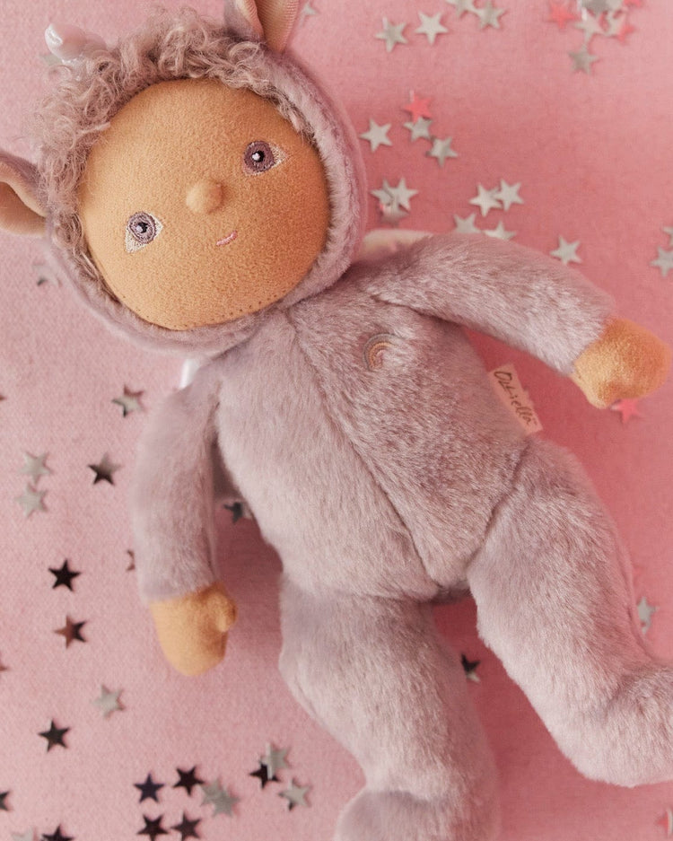 The Dinky Dinkum Doll Uma Unicorn Lilac by Dinkum Dolls is a soft, plush doll in a fuzzy lilac onesie with a hood and animal ears, featuring an embroidered face—perfect for cuddles and imaginative play.