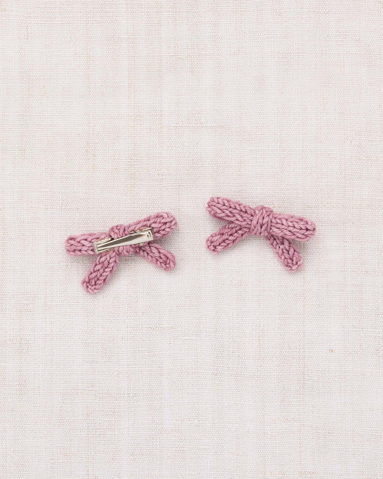 The goldie bow set in antique rose by misha + puff is displayed on a light beige fabric background. One bow reveals a metal alligator clip on the back, while the other shows the front, highlighting the soft merino wool texture.