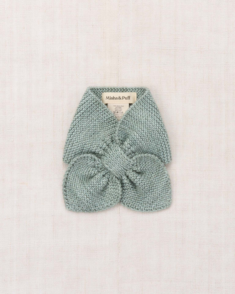 A soft, light blue Sledding Scarf in Onsen by misha + puff, crafted from luxurious Merino wool with a textured pattern, is folded neatly on a light beige fabric background. A small label reading misha + puff is visible at the top.