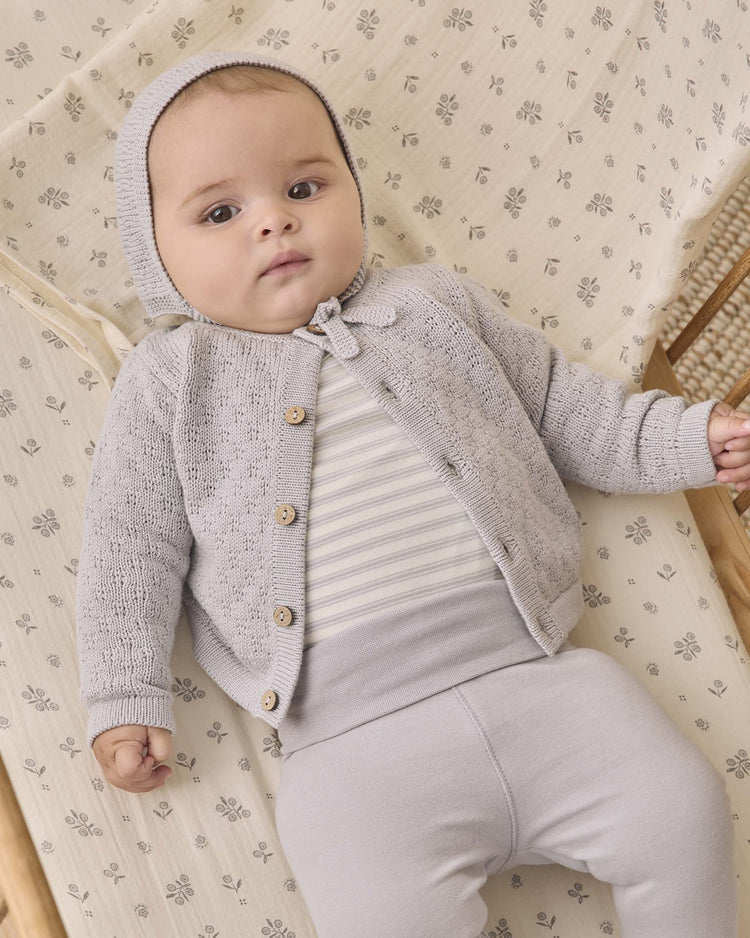 A baby lies on a patterned blanket, wearing the quincy mae side snap bodysuit + pant set in cloud stripe. The baby looks up with a calm expression.