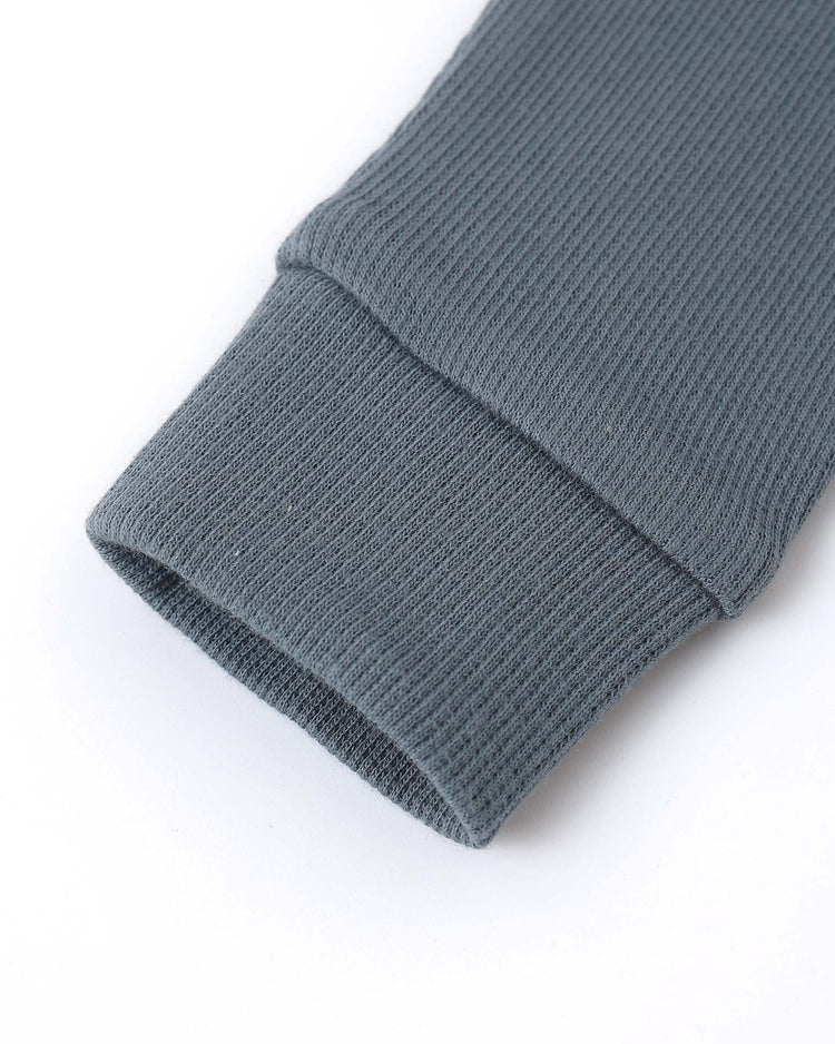 Close-up of a gray ribbed sweater sleeve cuff on a white background, showing fabric texture and stitching details, similar to the quality finish of quincy mae’s ribbed legging in ocean.