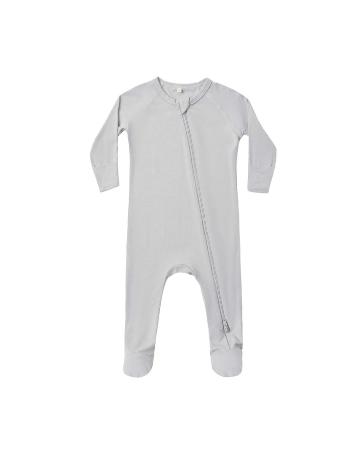 The bamboo zip footie in cloud by quincy mae is a light gray, long-sleeve baby onesie with footed bottoms, displayed flat on a white background. This cozy sleepwear features a diagonal zipper running from the neck down to one leg.
