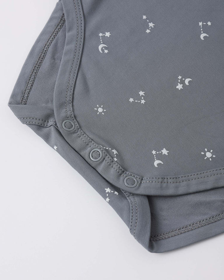 Close-up of the quincy mae bamboo short sleeve bodysuit in starlight, featuring snap buttons and a vintage nursery print with white stars, moons, and suns on soft gray fabric.