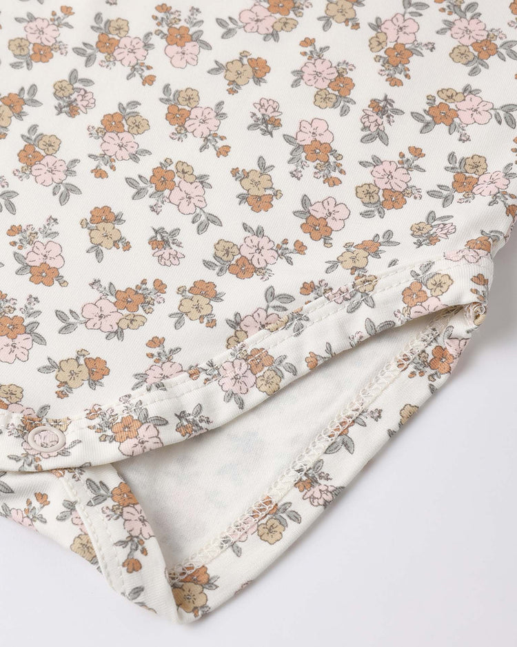 Close-up of the quincy mae bamboo short sleeve bodysuit in wildflower, featuring soft fabric with a delicate floral print in pastel pink, orange, and beige on off-white—vintage-inspired details perfect for your baby's cozy wardrobe.