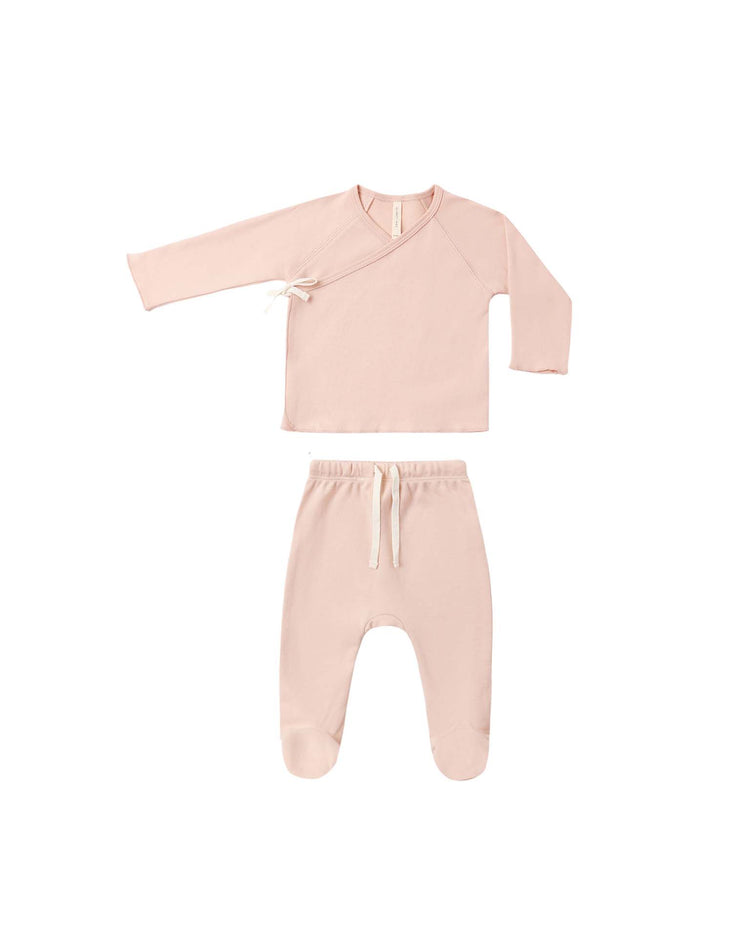 The wrap top + footed pant set in dusty rose by quincy mae is a pale pink, cozy baby set made from organic cotton. It features a long-sleeve newborn wrap top with a side tie and matching footed pants with a drawstring waist, displayed on a white background.