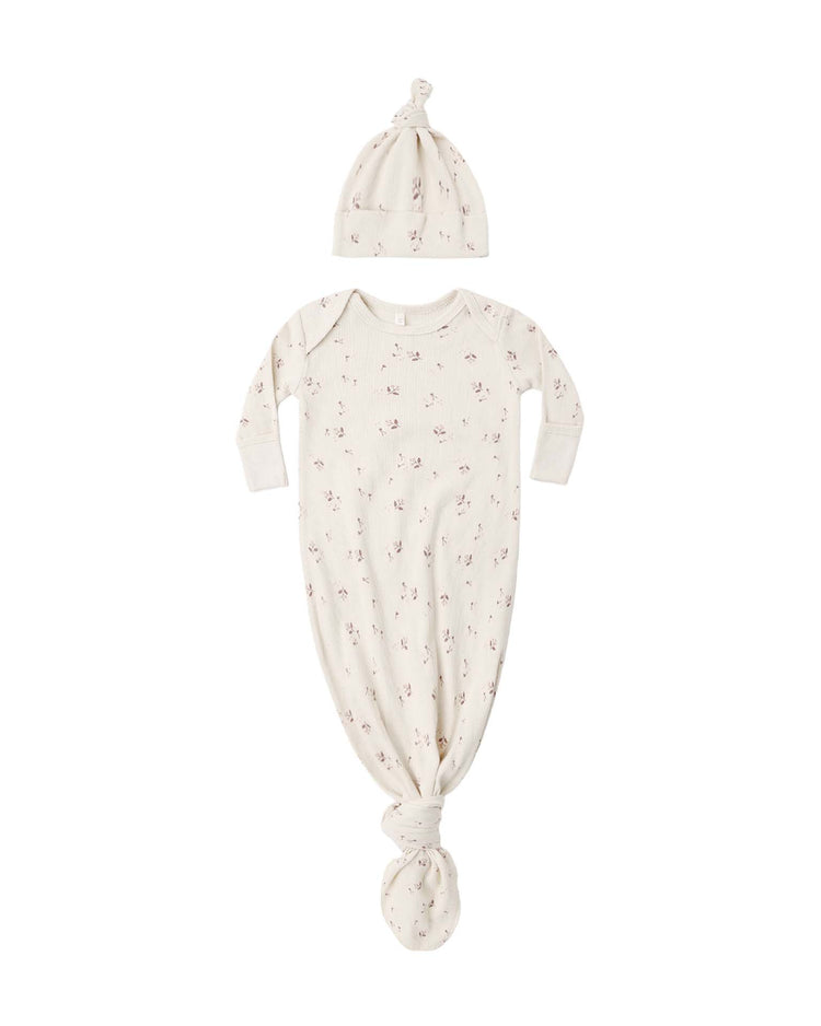 A cream-colored quincy mae knotted baby gown + hat set in fall ditsy featuring organic rib knit fabric with small floral prints is displayed laid flat on a white background; the gown includes long sleeves with fold-over hand mitts and a knotted bottom, complemented by a matching beanie hat.
