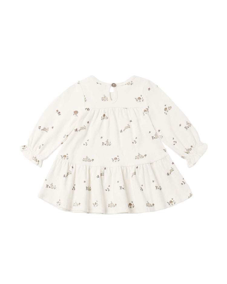 A white long-sleeve tiered jersey dress in bunnies by quincy mae, crafted from soft organic cotton with a ruffled hem and a subtle bunny print. The back features a round button closure at the neckline, making it perfect for pairing with baby bloomers.