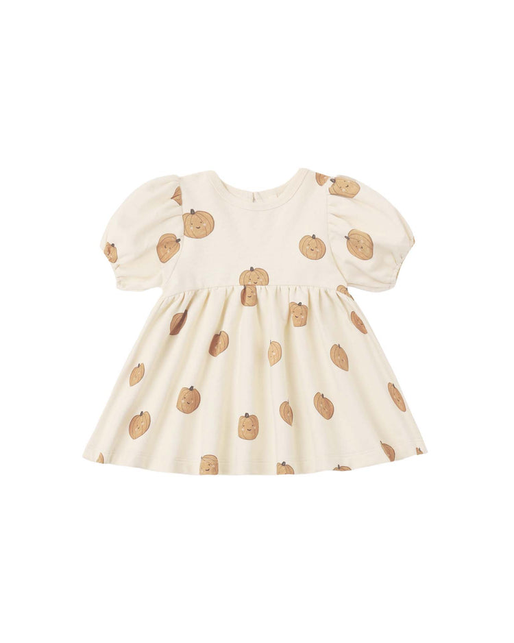 The “darla dress in pumpkins” by quincy mae is a cream-colored organic cotton babydoll dress with short puff sleeves and an all-over smiling brown pumpkin print. It features a round neckline and a flared waist, shown against a plain white background.