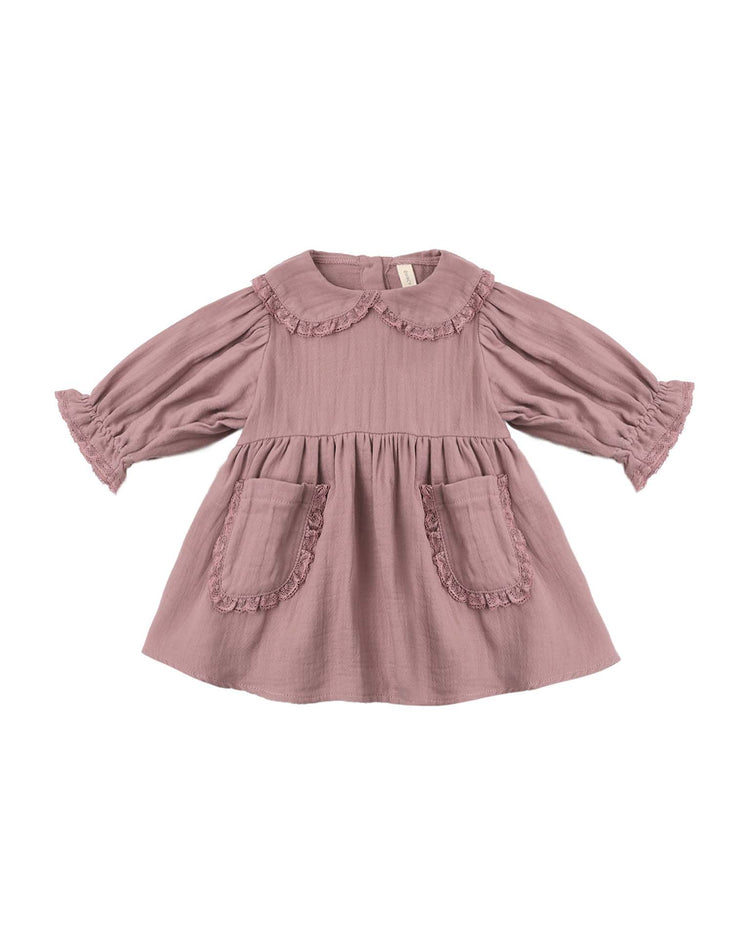 The marisol dress in mulberry by quincy mae is an organic cotton, long-sleeve dress in a delicate mauve shade, designed with a scalloped Peter Pan collar, ruffled cuffs, and two front pockets adorned with ruffle trim, shown laid flat on a white background.