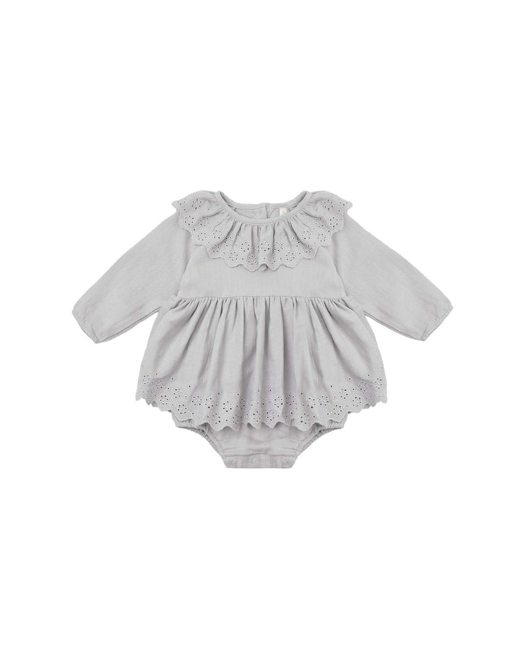 The thalia romper in cloud by quincy mae is a light gray, long-sleeve organic cotton baby romper featuring a scalloped eyelet ruffle collar and matching hem detail on the skirt. It has a gathered waist, delicate embroidery accents, and convenient snap closures at the bottom.