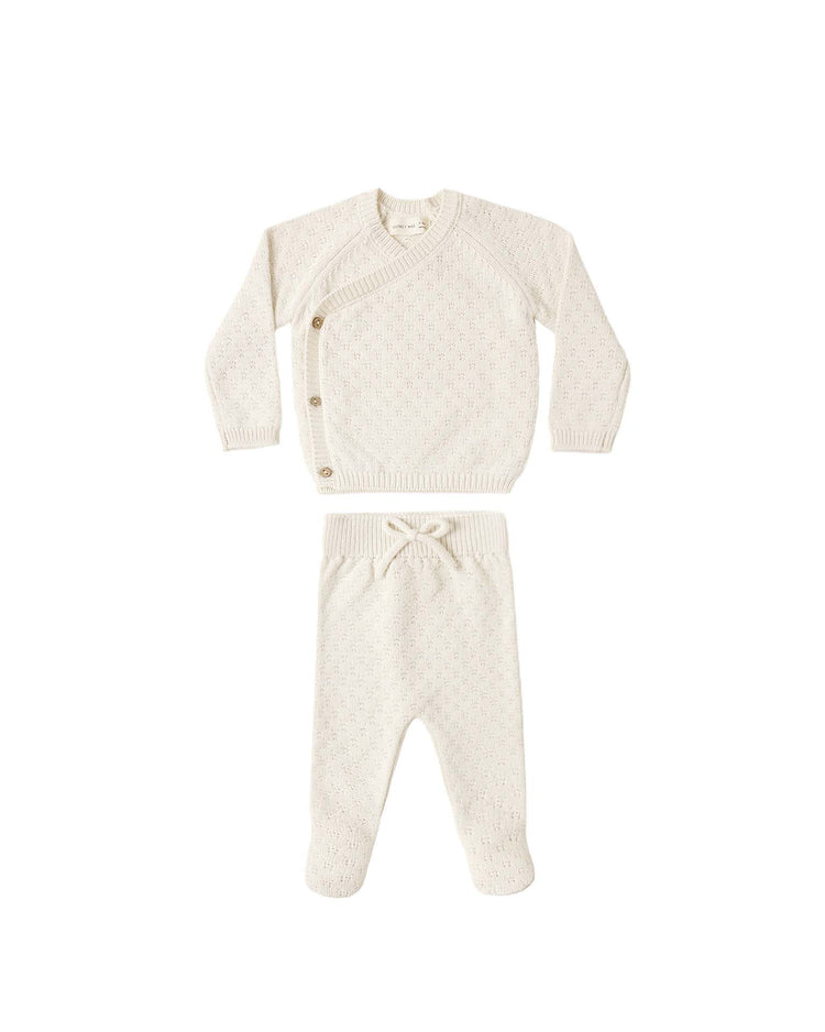 The quincy mae knit wrap top + pant set in natural features a cream-colored, long-sleeve wrap-style sweater with side buttons and matching knit footed pants with a drawstring waist, both crafted from organic cotton baby clothes and displayed on a plain white background.