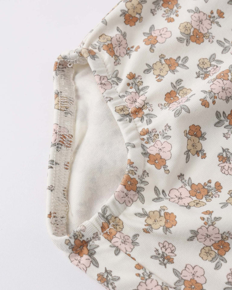 Close-up of the quincy mae bamboo babydoll dress in wildflower, featuring a pink, orange, and gray floral pattern on white fabric. The image highlights the edge and seam, possibly part of ruffle sleeves.
