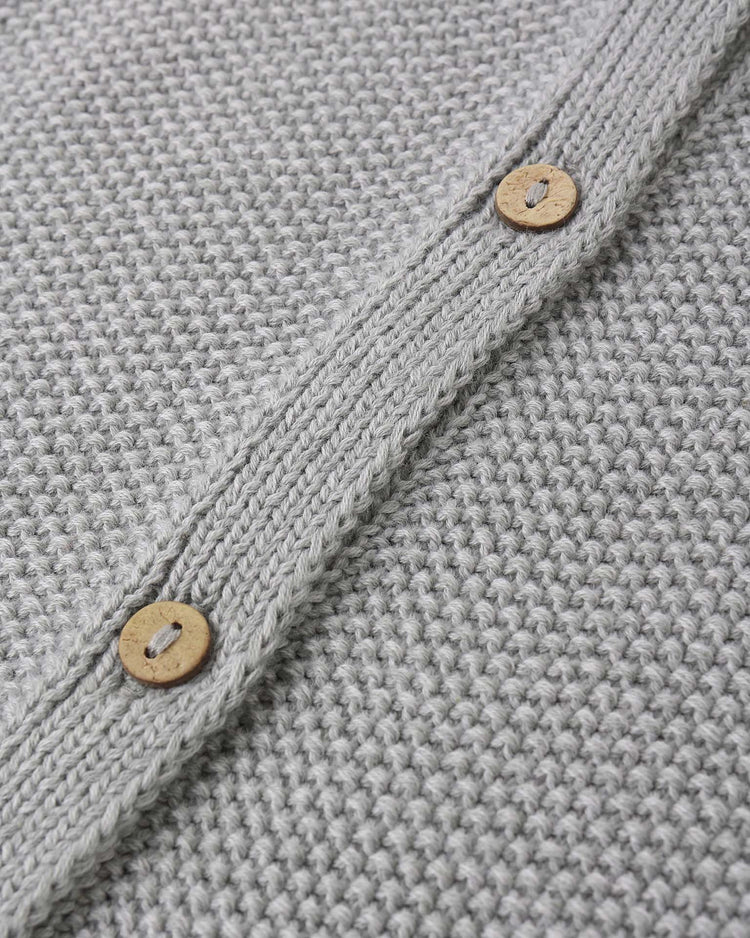 Close-up of the "knit jumpsuit in heathered sky" by quincy mae, featuring light gray organic cotton knit fabric with two round wooden buttons on a ribbed edge.
