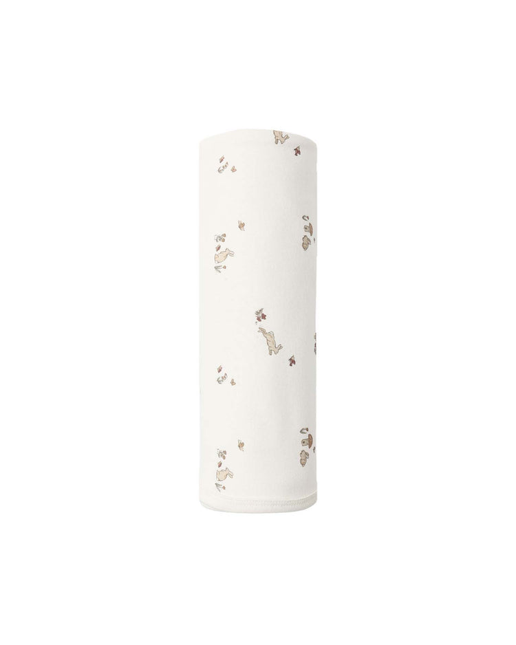 Swaddle in Bunnies by quincy mae is shown rolled up vertically against a plain white background, featuring a soft white fabric adorned with small, light brown bunny illustrations and paw prints.
