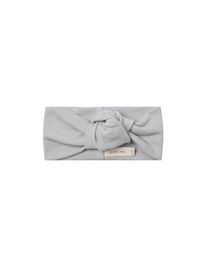 The knotted headband in cloud by quincy mae is a light gray organic cotton accessory featuring a central knot design and a small Quincy Mae label on the front, making it an adorable choice for babies.