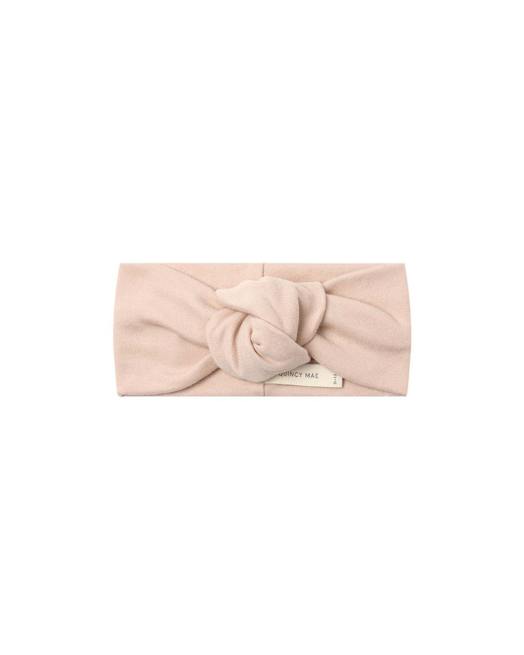 The knotted headband in dusty rose by quincy mae is crafted from soft organic cotton in a gentle light pink shade, featuring a central knot and a small rectangular label near the bottom edge.