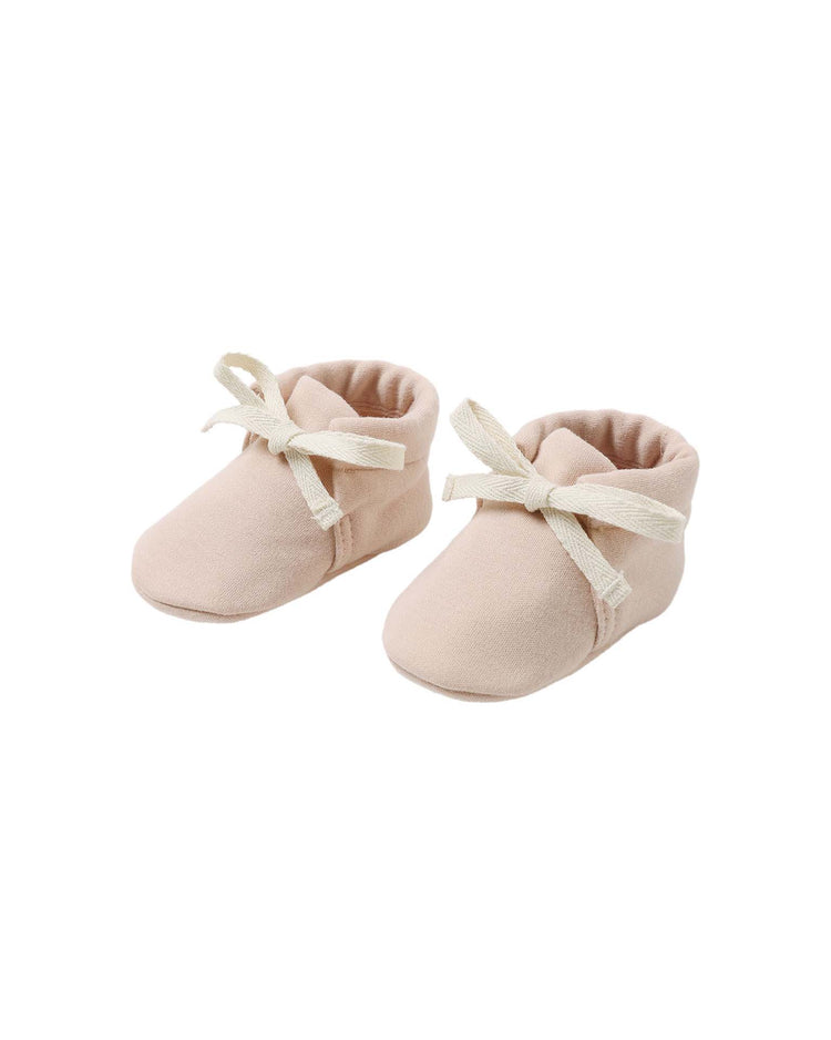 A pair of soft, dusty rose organic cotton baby booties by quincy mae, featuring cream-colored fabric laces, displayed on a white background.