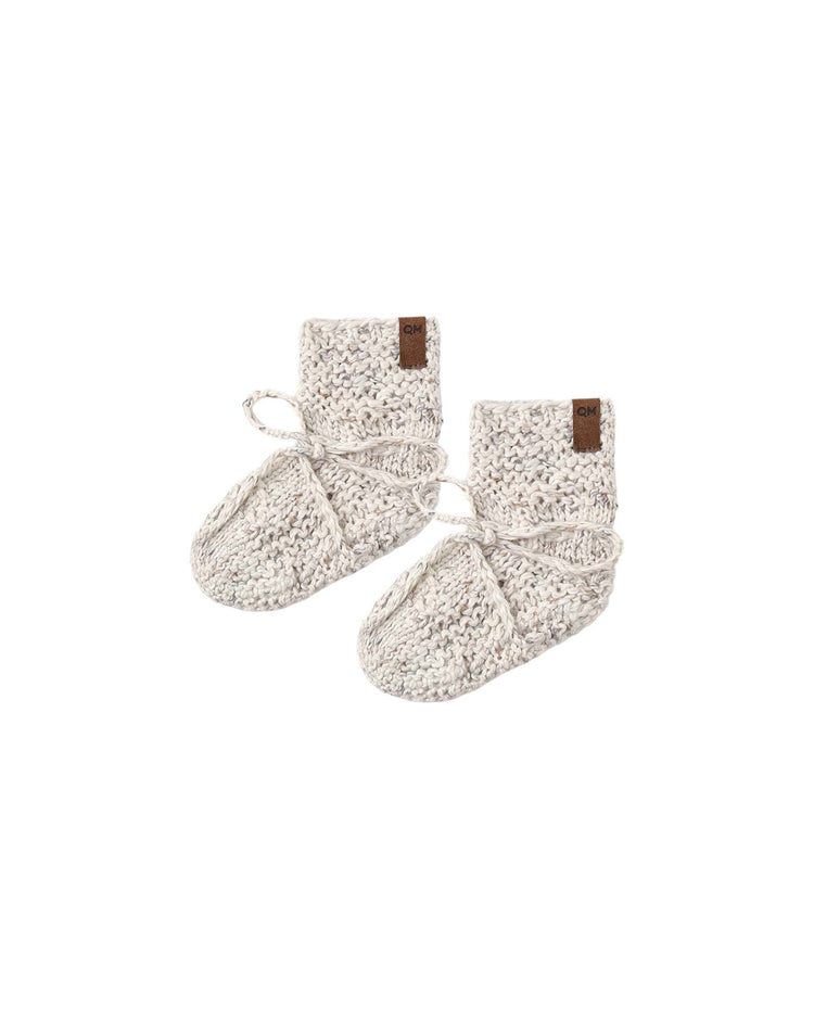 A pair of knit booties in natural confetti by quincy mae, crafted from soft organic cotton with folded cuffs and ties, featuring small brown tags on the cuffs, displayed on a white background.