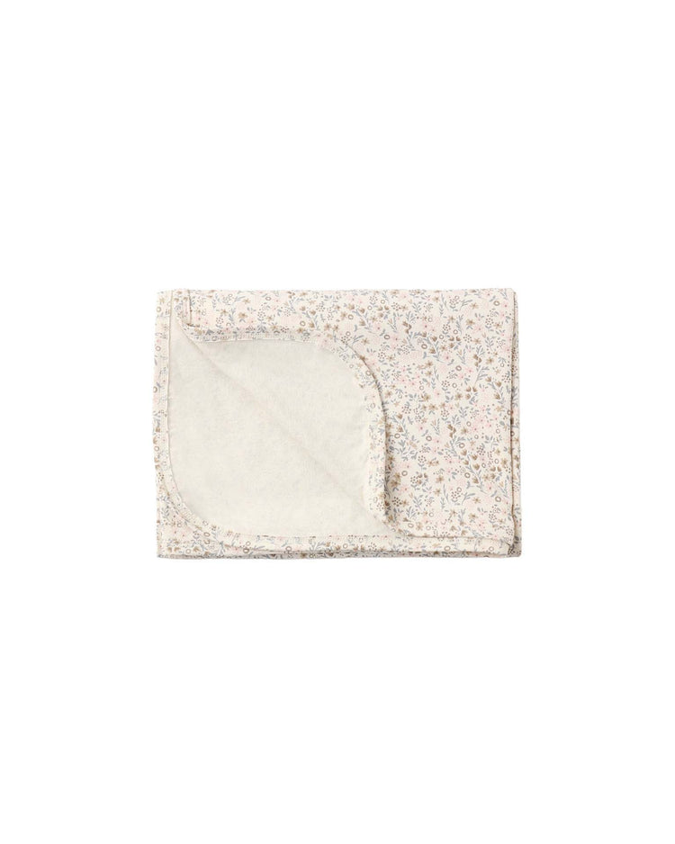 The bamboo swaddle in bloom by quincy mae is a soft, folded baby blanket made from gentle bamboo fabric, featuring a delicate bloom print on the outside and a plain, light-colored inner lining. One corner is flipped to reveal the contrasting inside texture.