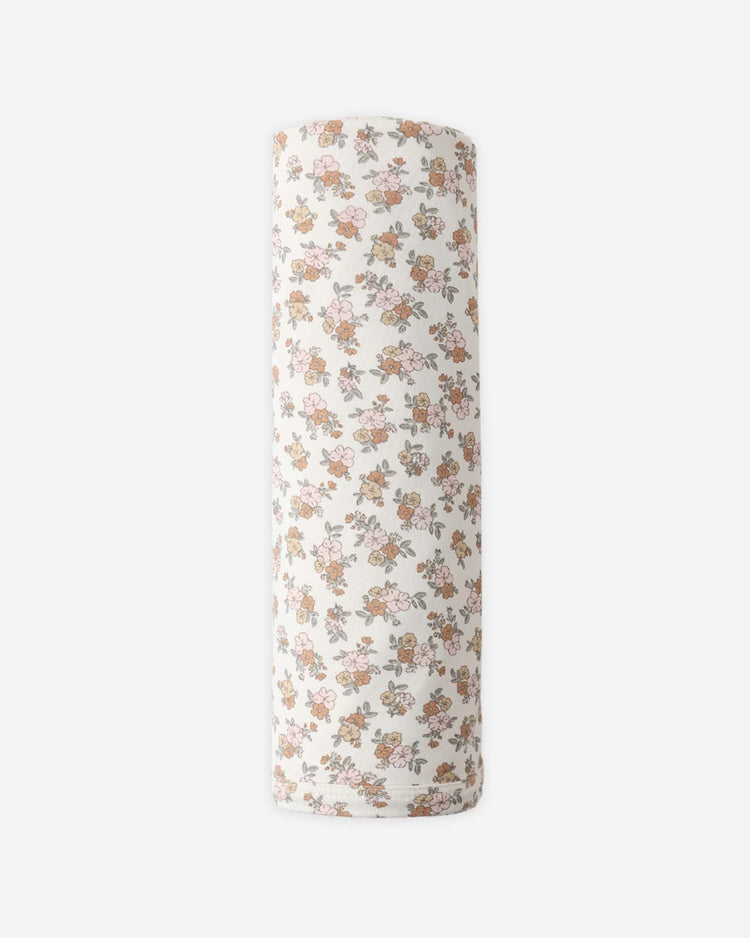 The quincy mae bamboo swaddle in wildflower is a rolled-up white baby wrap made from soft bamboo, featuring a delicate print of pink, yellow, and brown blooms with green leaves, shown on a plain white background.