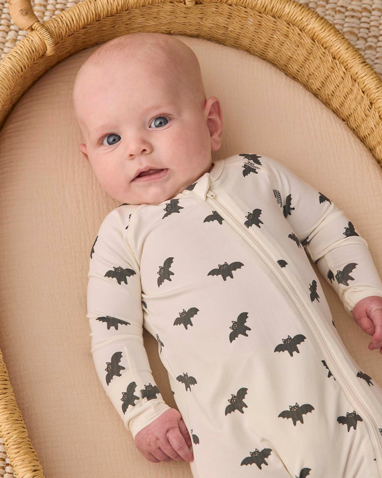 A baby lies in a basket, wearing the quincy mae bamboo zip footie in bats, gazing upward with wide blue eyes.