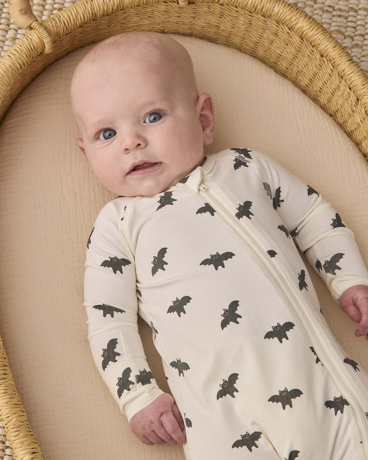 A baby lies in a basket, wearing the quincy mae bamboo zip footie in bats, gazing upward with wide blue eyes.