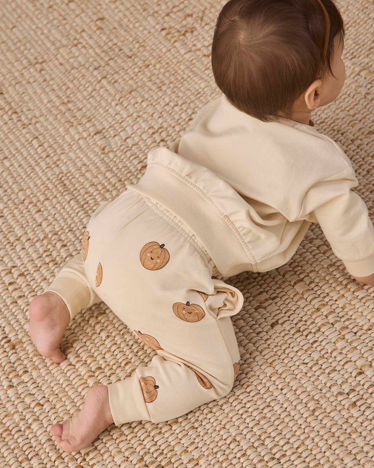 A baby in Quincy Mae’s relaxed fleece sweatpant in pumpkins crawls on a textured woven rug, facing away from the camera.