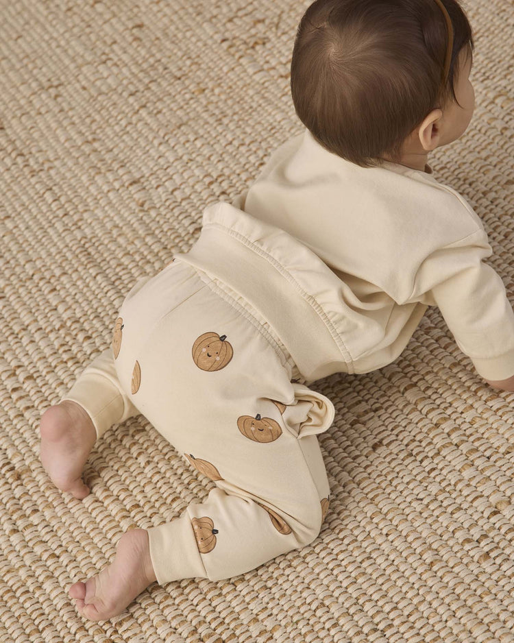 A baby in Quincy Mae’s relaxed fleece sweatpant in pumpkins crawls on a textured woven rug, facing away from the camera.