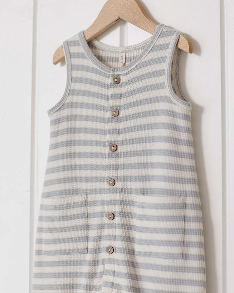 The quincy mae waffle jumpsuit in sky stripe features a sleeveless, button-down design with gray and white stripes, front pockets, and wooden buttons—ideal for a baby’s transitional wardrobe.