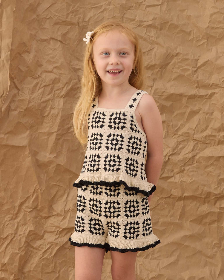 A young girl wearing rylee + cru's crochet bow clips in ivory smiles, standing in front of a crumpled brown paper background.