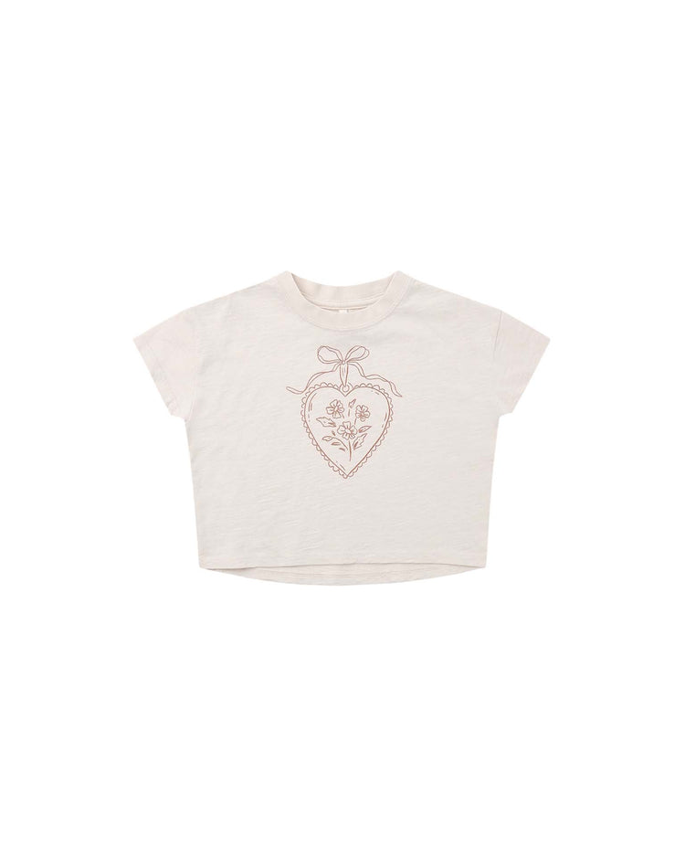 PREORDER the rylee + cru boxy tee in heart locket—a white, short-sleeve crop top made from 100% cotton. Featuring a simple brown line art design of a heart-shaped wreath with flowers and a bow, centered on the chest, this tee combines comfort with effortless style in a relaxed boxy fit.