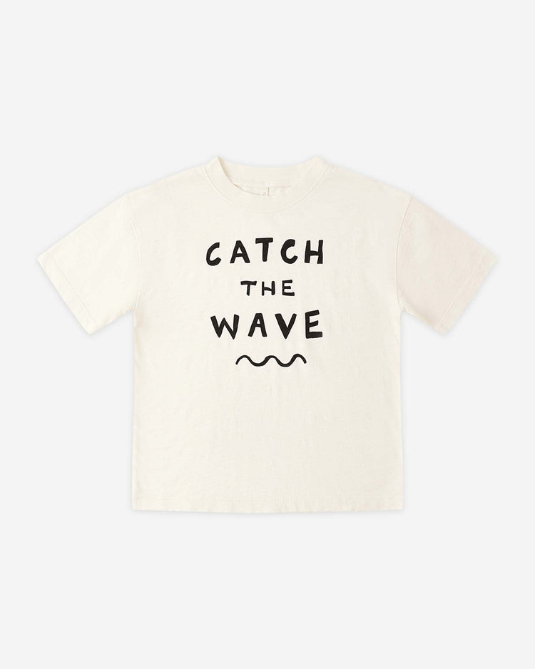 The "relaxed tee in catch the wave" by rylee + cru is a cream cotton jersey shirt featuring "CATCH THE WAVE" in bold black letters above a black wavy line, displayed flat on a white background.