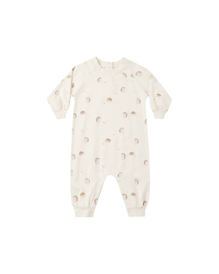 The rylee + cru raglan jumpsuit in hedgehog is a cream-colored French terry romper with long sleeves and legs, featuring a subtle hedgehog print with tiny moons. It includes snap closures at the legs and cuffs at the wrists and ankles.