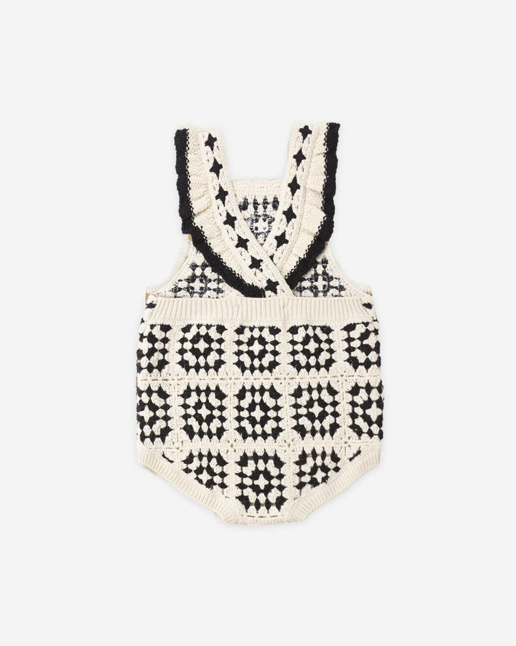 The "crochet romper in abstract" by rylee + cru features a cream and black granny square pattern, crisscross straps, and ruffled trim for vintage flair. Made from 100% cotton for comfort and style.
