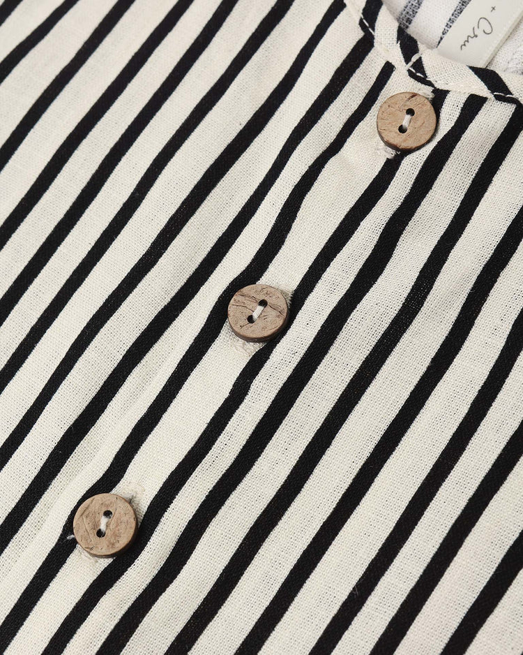 Close-up of the rylee + cru mavrick romper in wavy stripe, showcasing black and white vertical stripes and three round wooden buttons down the center. The linen viscose fabric is seen as part of the romper's design.