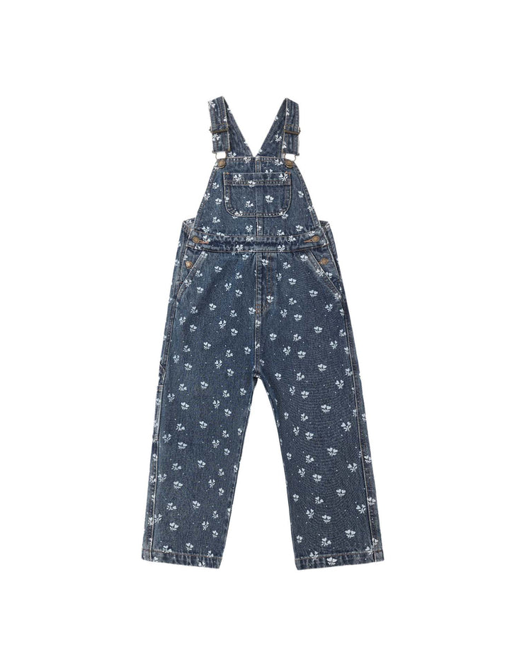 The “utility overall in heart ditsy” by rylee + cru is a blue indigo denim children’s overall featuring adjustable shoulder straps, a front chest pocket, and an all-over small white heart ditsy print. The overalls are displayed laid flat on a white background.