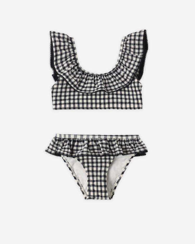 The rylee + cru margot bikini in black gingham features a ruffle collar neckline and waist ruffles, with UPF 50+ protection, displayed flat on a white background to highlight its chic style.