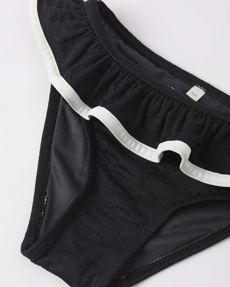 The daisy bikini in black from rylee + cru features a white ruffle waistband and is crafted from recycled polyamide, shown on a white surface.