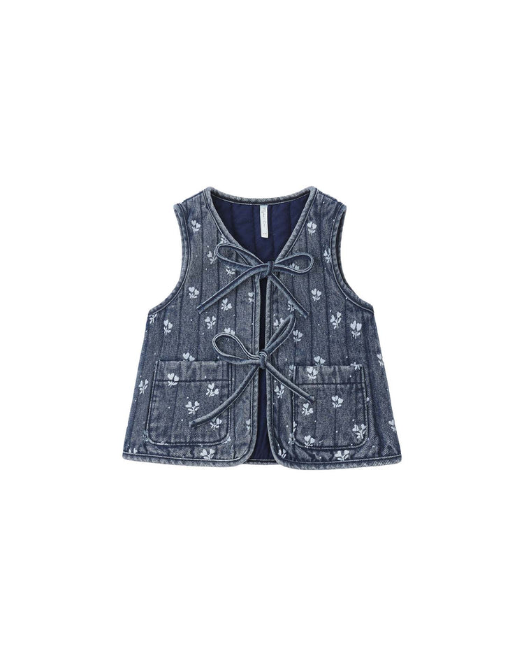 The “denim vest in heart ditsy” by rylee + cru is a sleeveless 100% cotton denim vest displayed on a white background, featuring two front pockets, subtle white floral embroidery, quilted panels for added texture, and two front tie closures.
