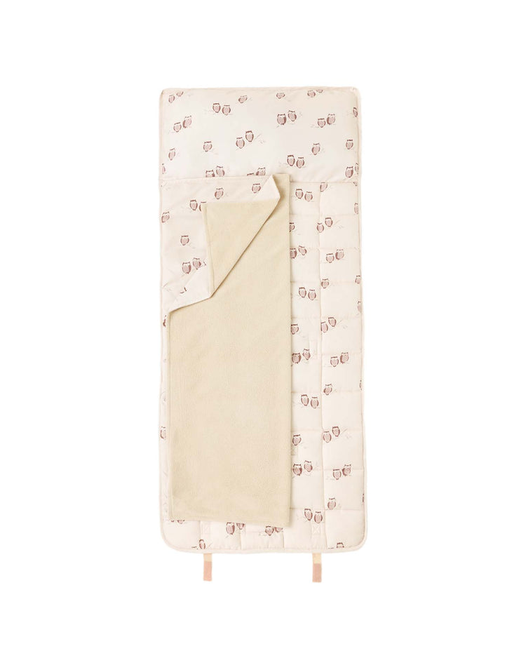 A cream-colored, rectangular nap mat in owls by rylee + cru, featuring a pattern of small animal faces on the outer fabric, a beige inner micro-fleece blanket, and a removable pillow, shown laid flat on a white background.